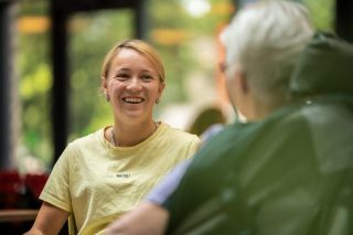 Blije jonge zorgmedewerker in gesprek met een bewoner in een rolstoel